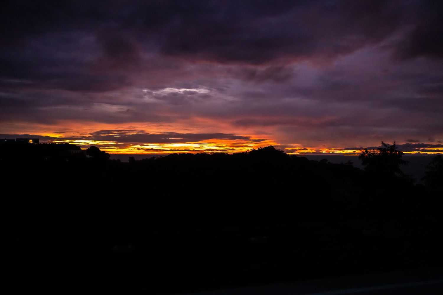 Dramatic sunset sky with dark clouds silhouetted against vibrant orange and purple horizon.
