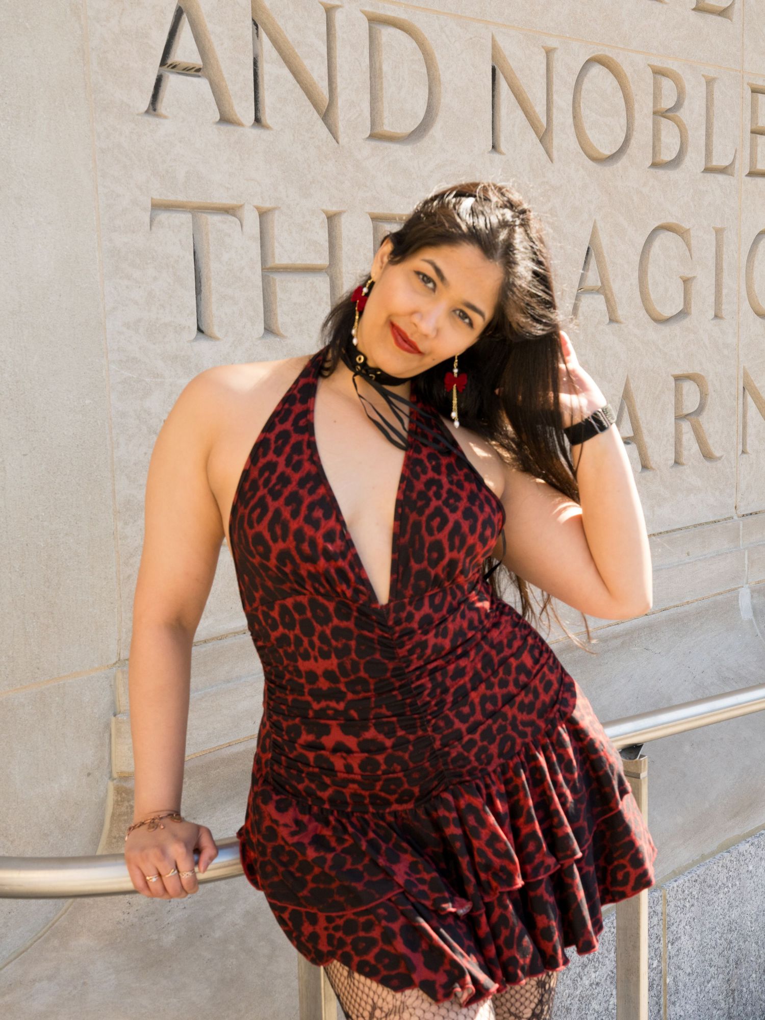 Woman in red leopard print halter dress poses confidently outdoors against an engraved stone wall.