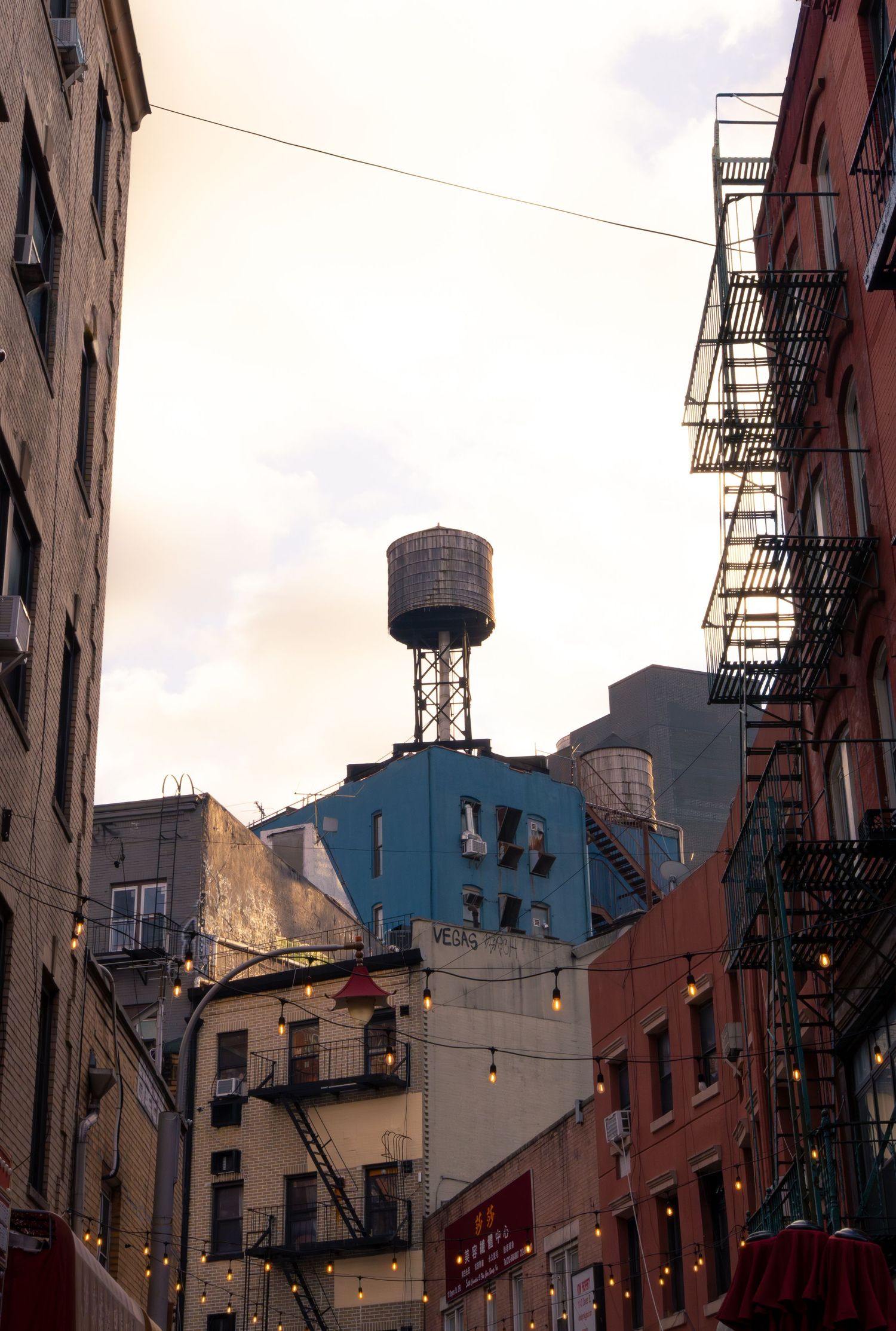 Urban cityscape with fire escapes and water towers on buildings against an overcast sky in New York City.