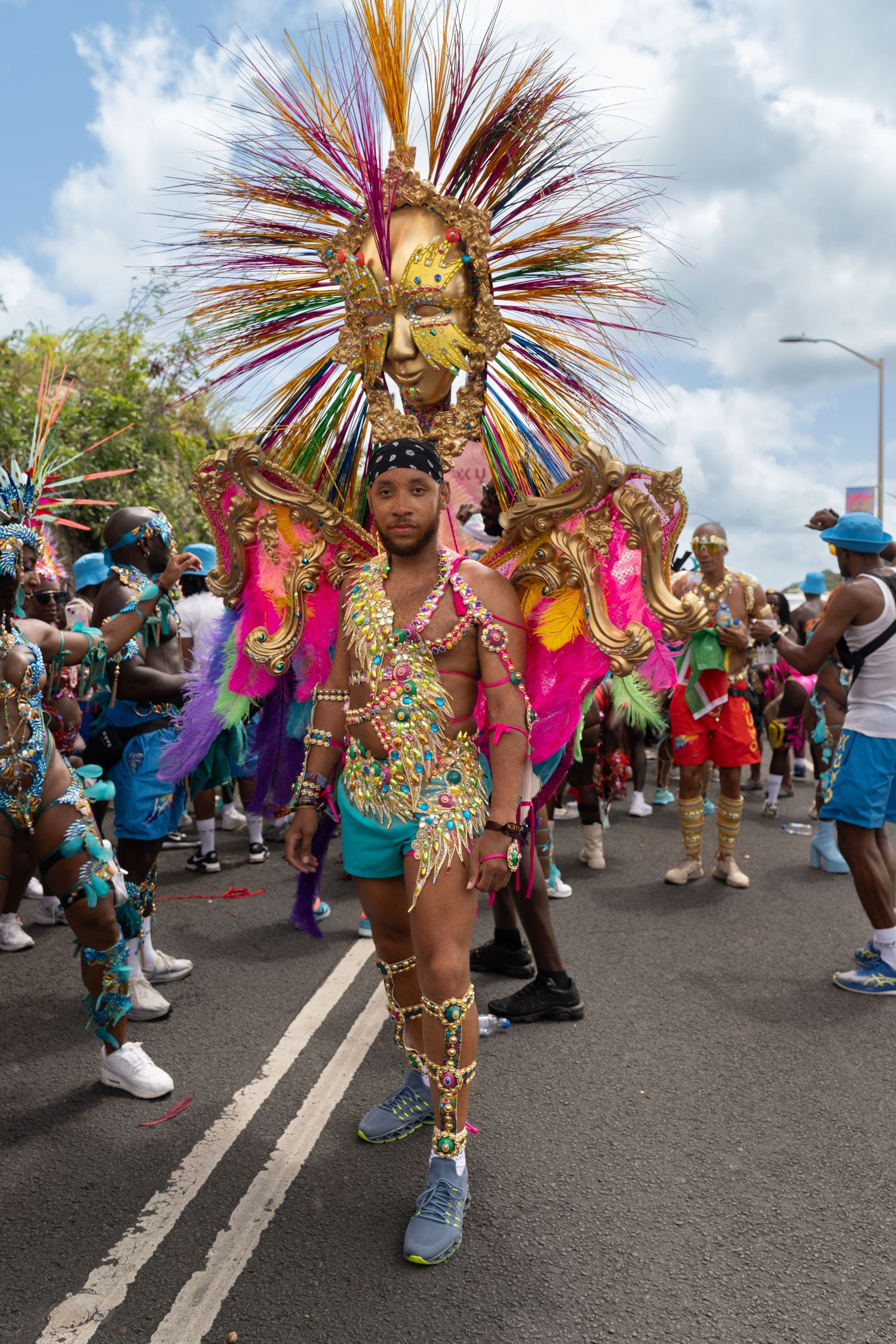 Carnival dancers in vibrant feathered costumes perform during a street parade celebration with onlookers watching.