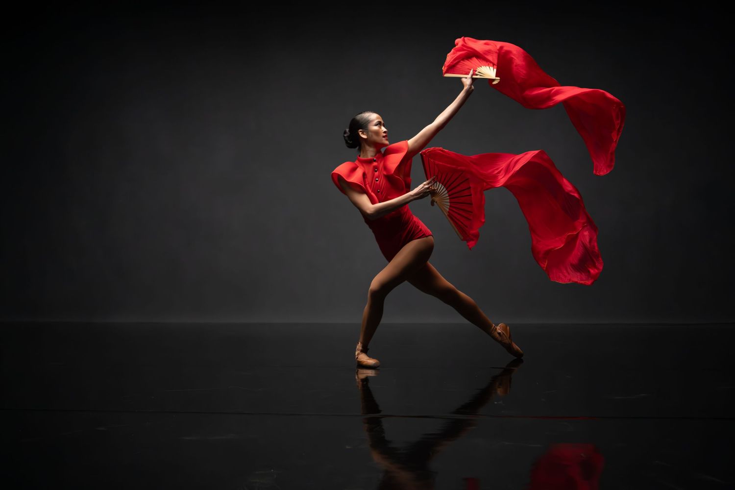 Dancer leaps gracefully with billowing red silk fabric against black backdrop.