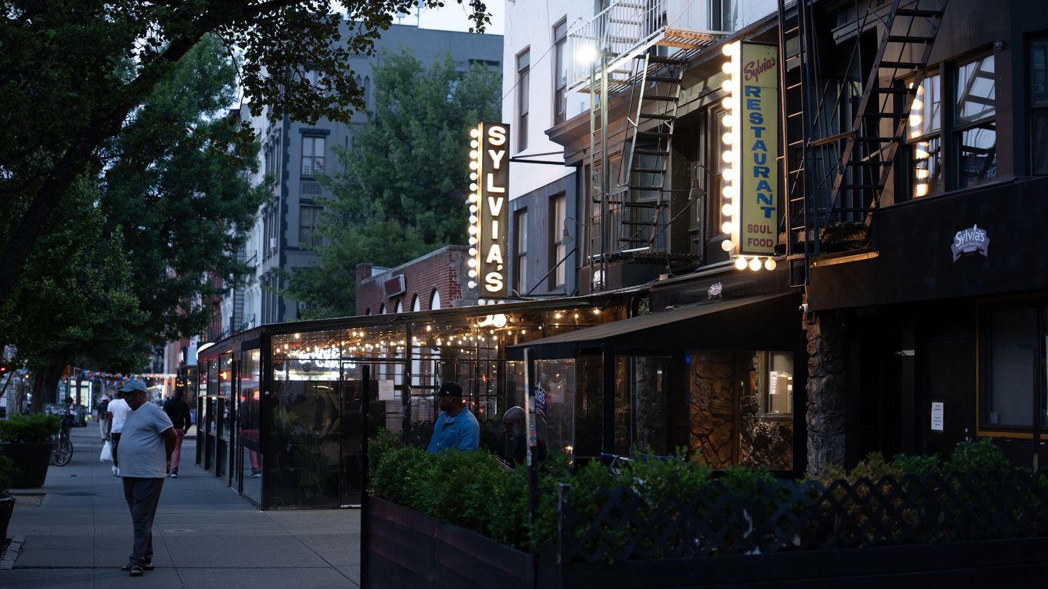 Panoramic view of a city street with shops and restaurants at dusk.