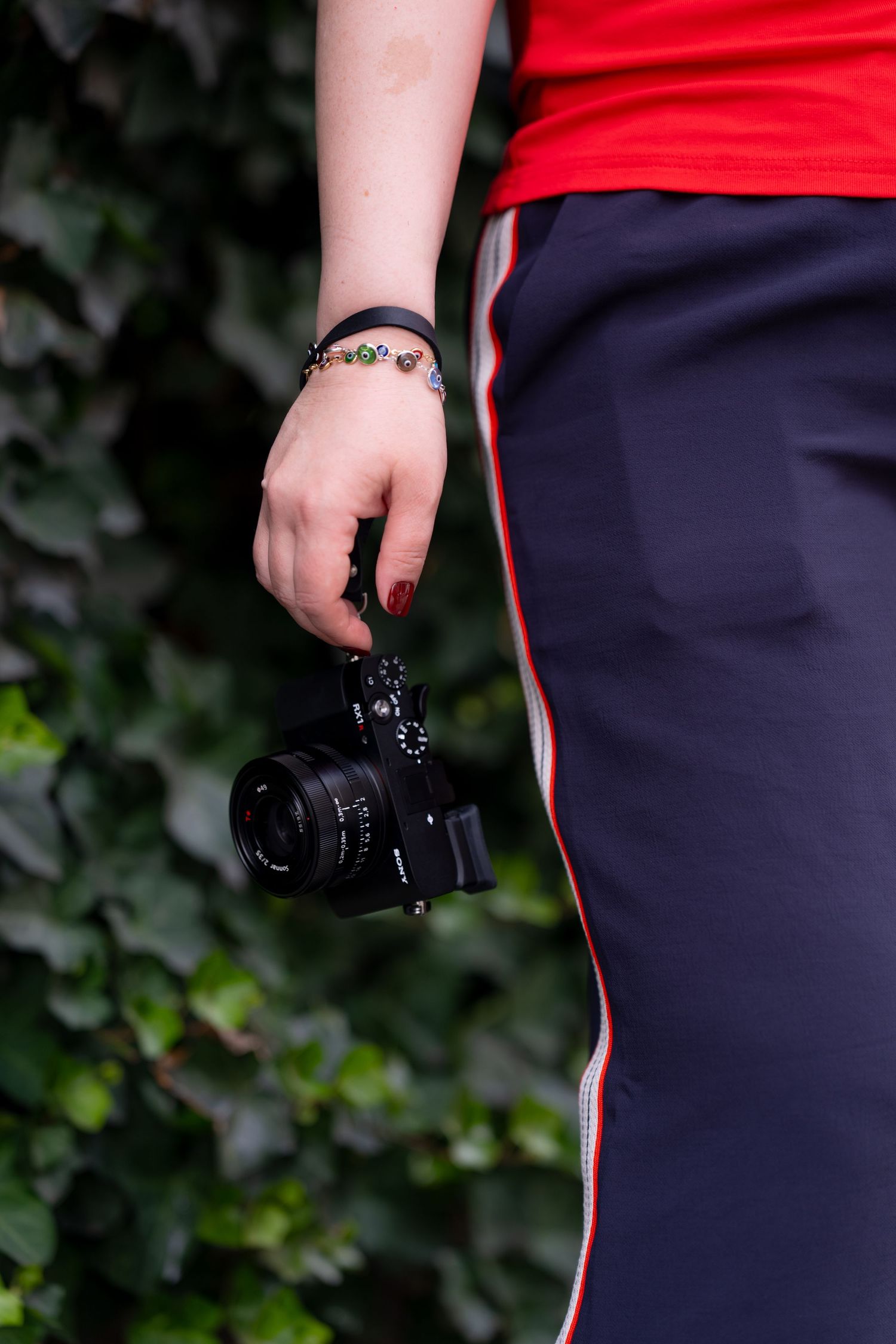Close-up view of hands holding a black DSLR camera against a dark background with green foliage.