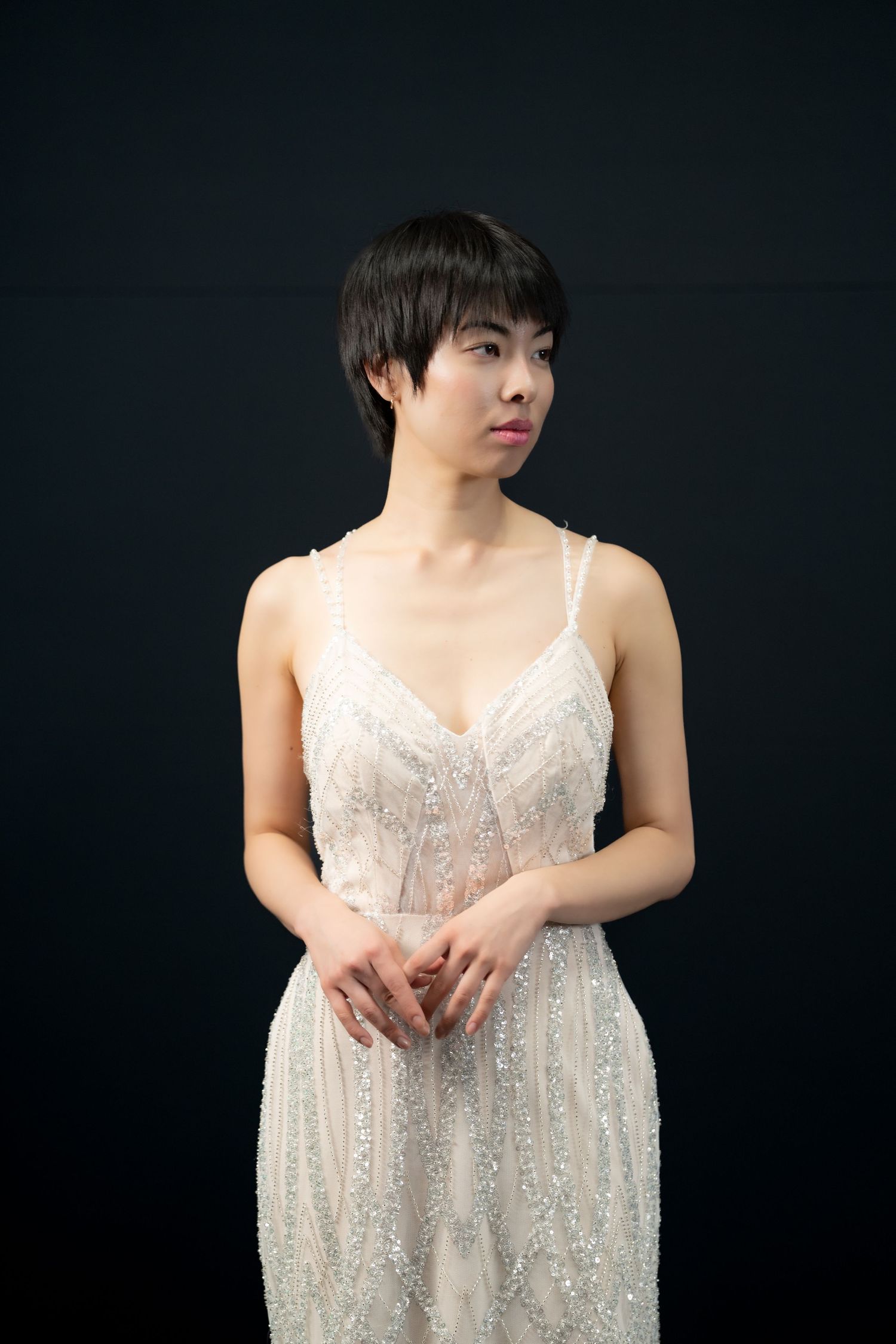 Figure in a sparkly white dress poses against dark background in artistic portrait series.