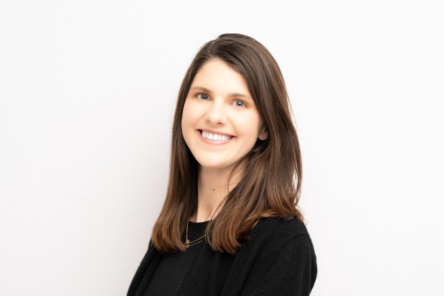 Professional headshot of a person with dark hair wearing a black top against a light background.