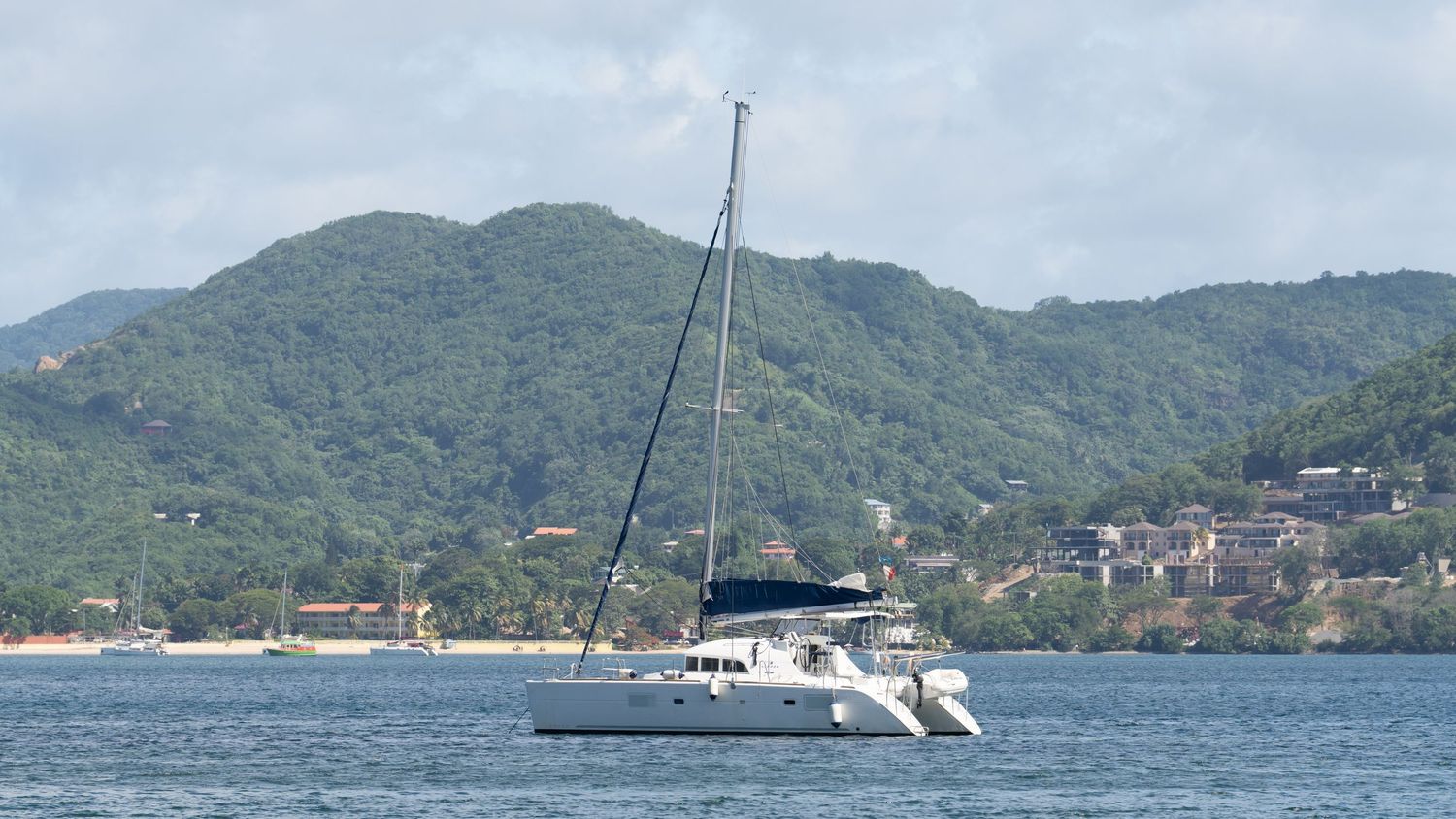 Panoramic view of sailboats anchored near mountainous coastline.