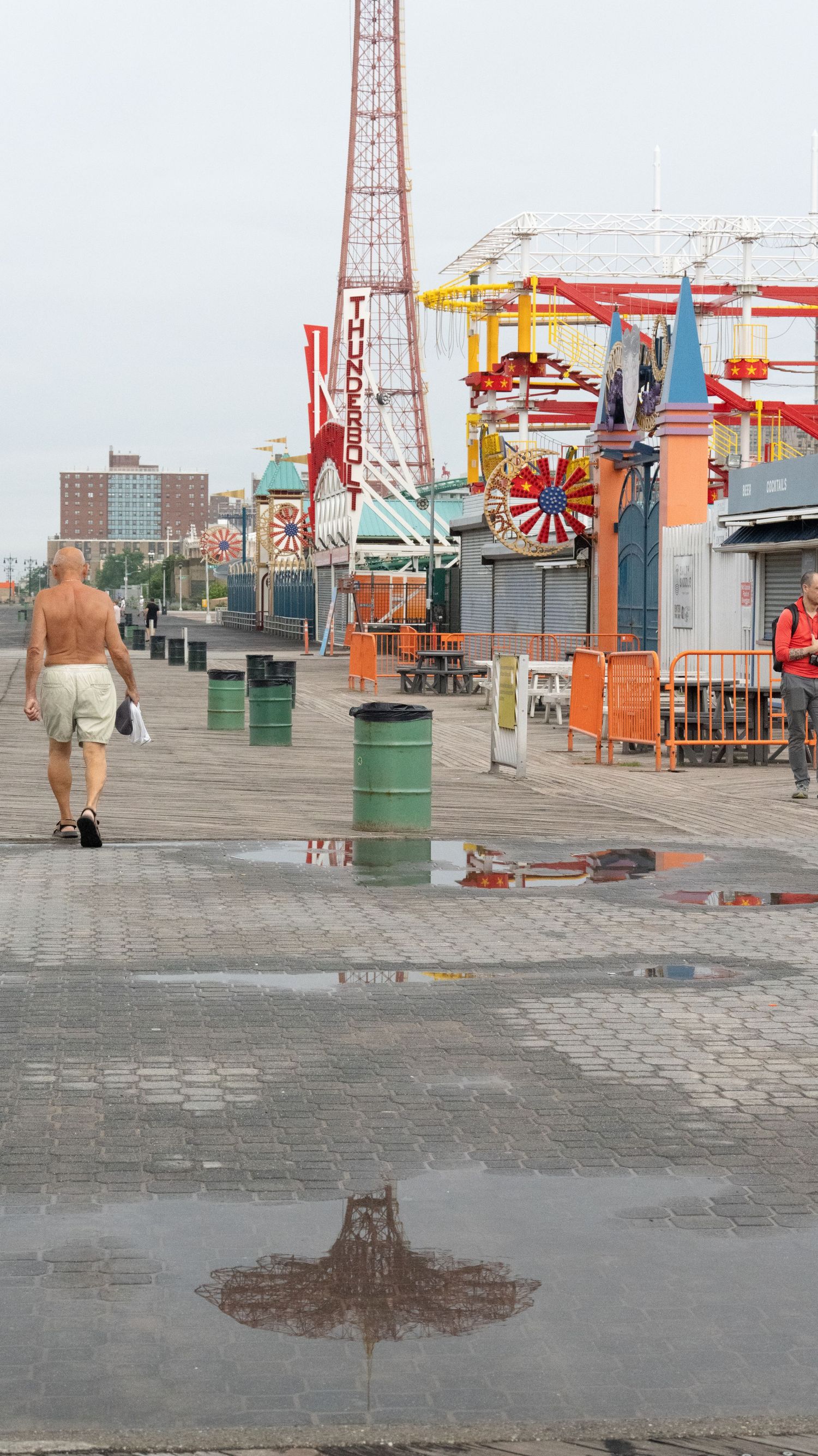 Amusement park boardwalk with carnival rides and parachute jump tower on a cloudy day.