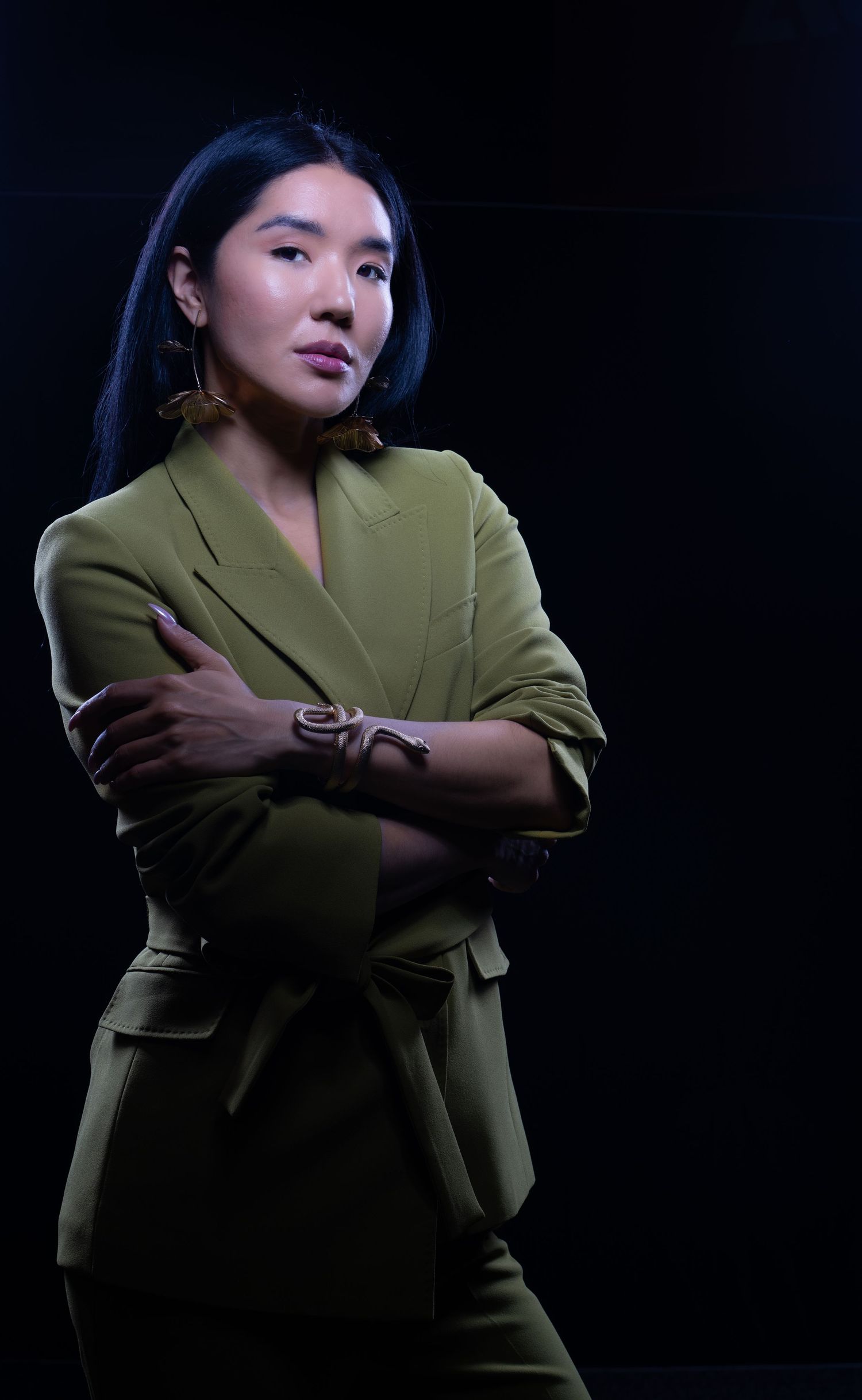 Dramatic portrait in olive green blazer against dark background with moody lighting.