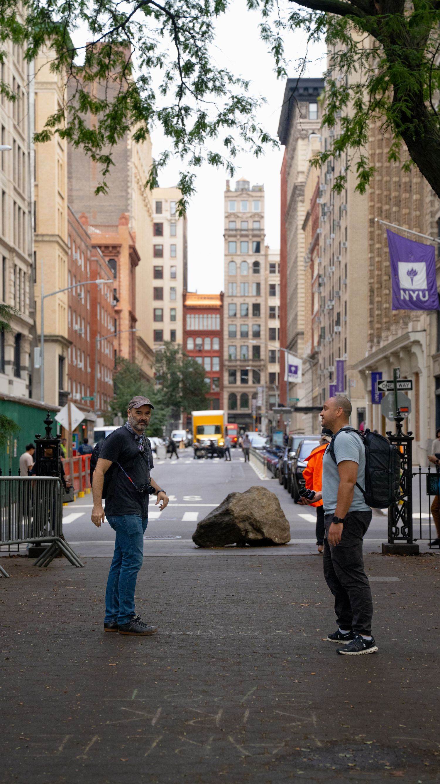 People skateboarding on a wide sidewalk near NYU campus buildings in New York City.