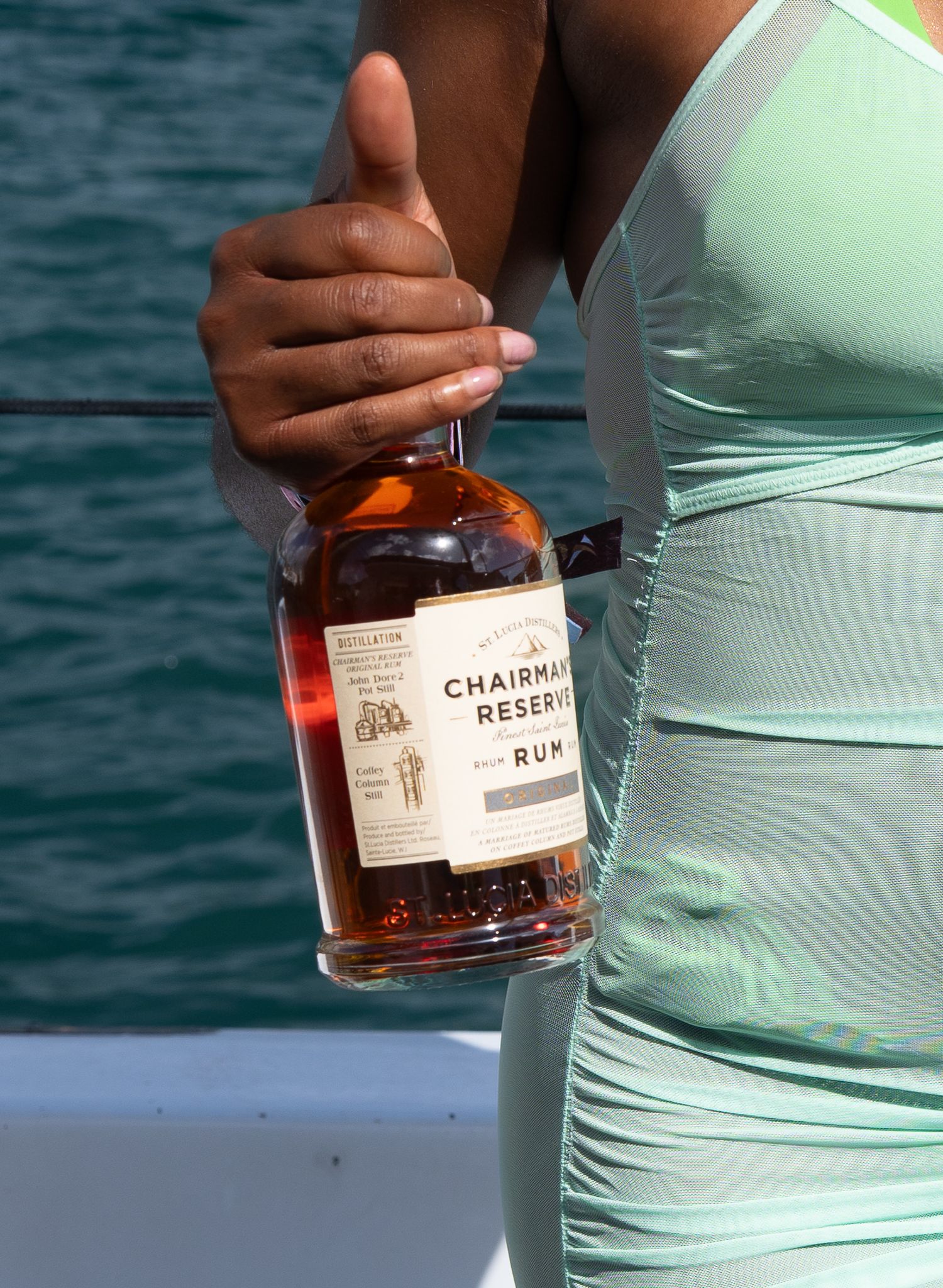 Bottles of Chairman's Reserve rum being held against a turquoise ocean background.