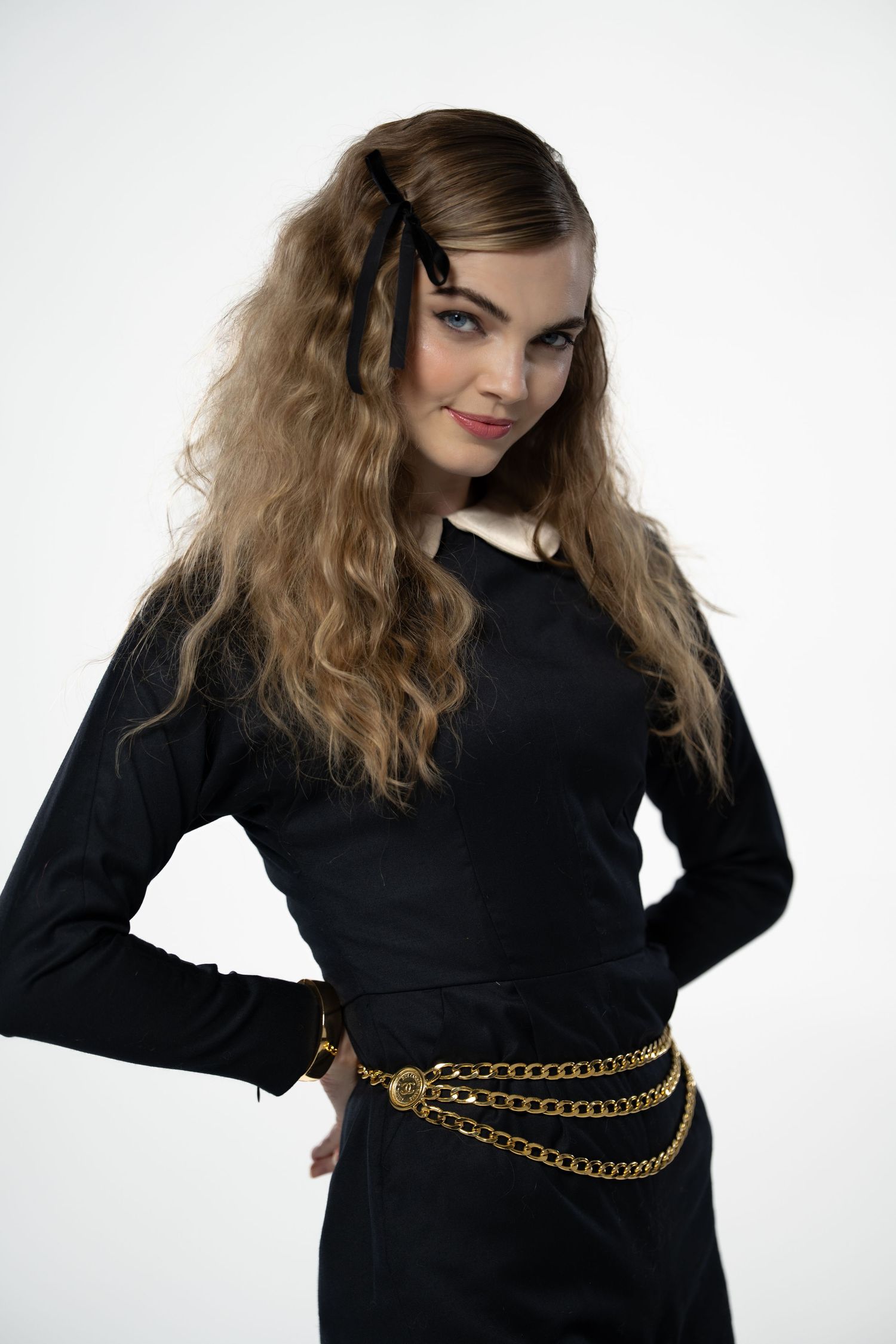 Model wearing black top with gold chain belt poses against white background.