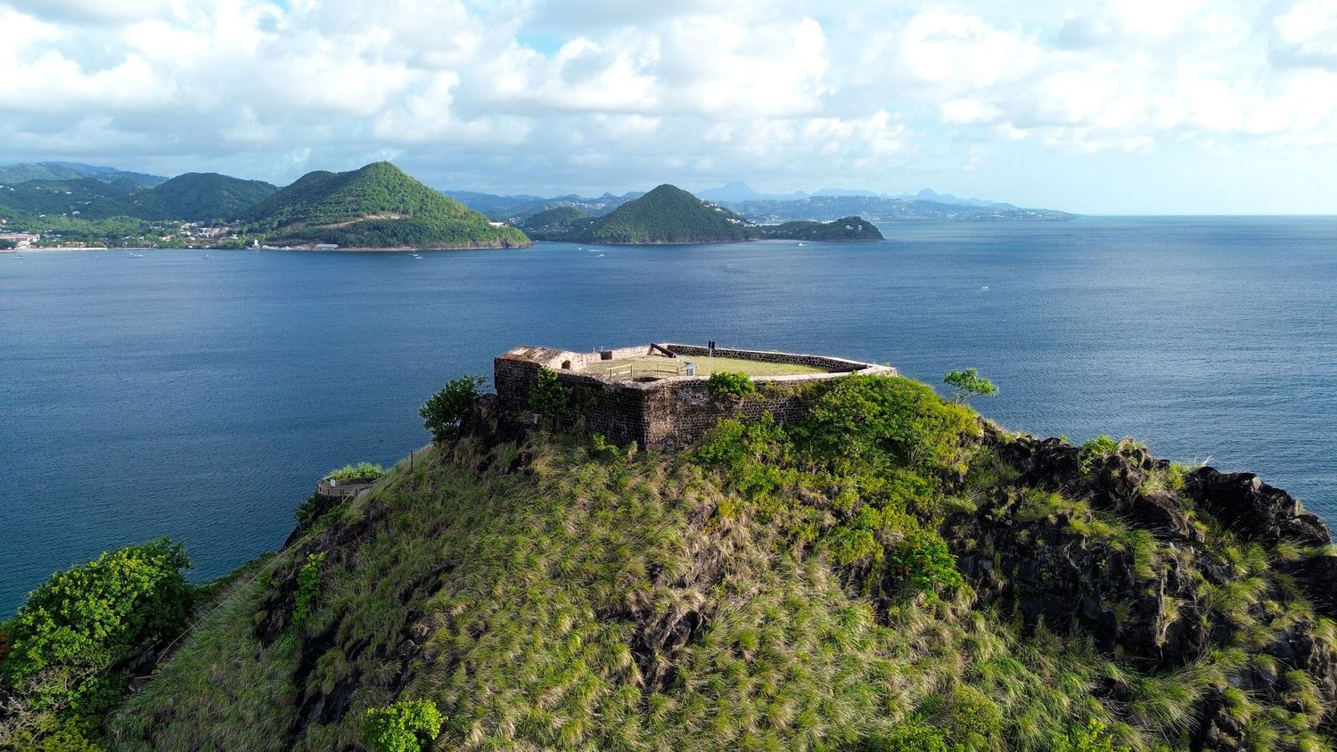 Panoramic view of lush green coastal mountains rising above turquoise ocean waters.