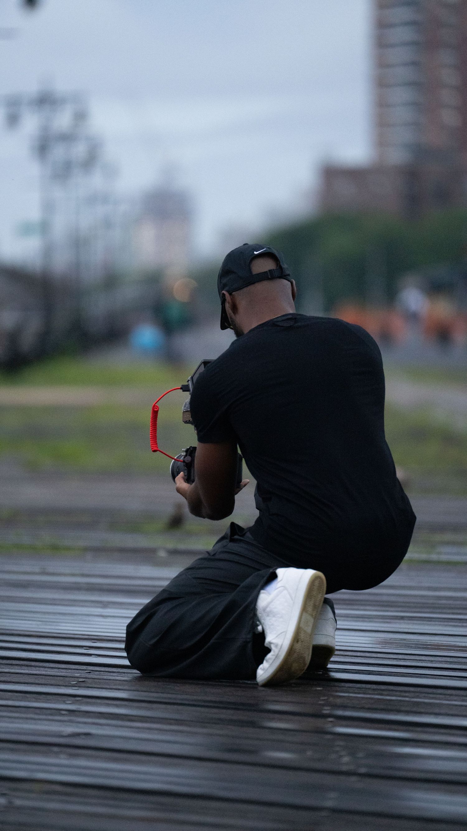 Camera operator shooting from low angle on wooden platform with urban background.