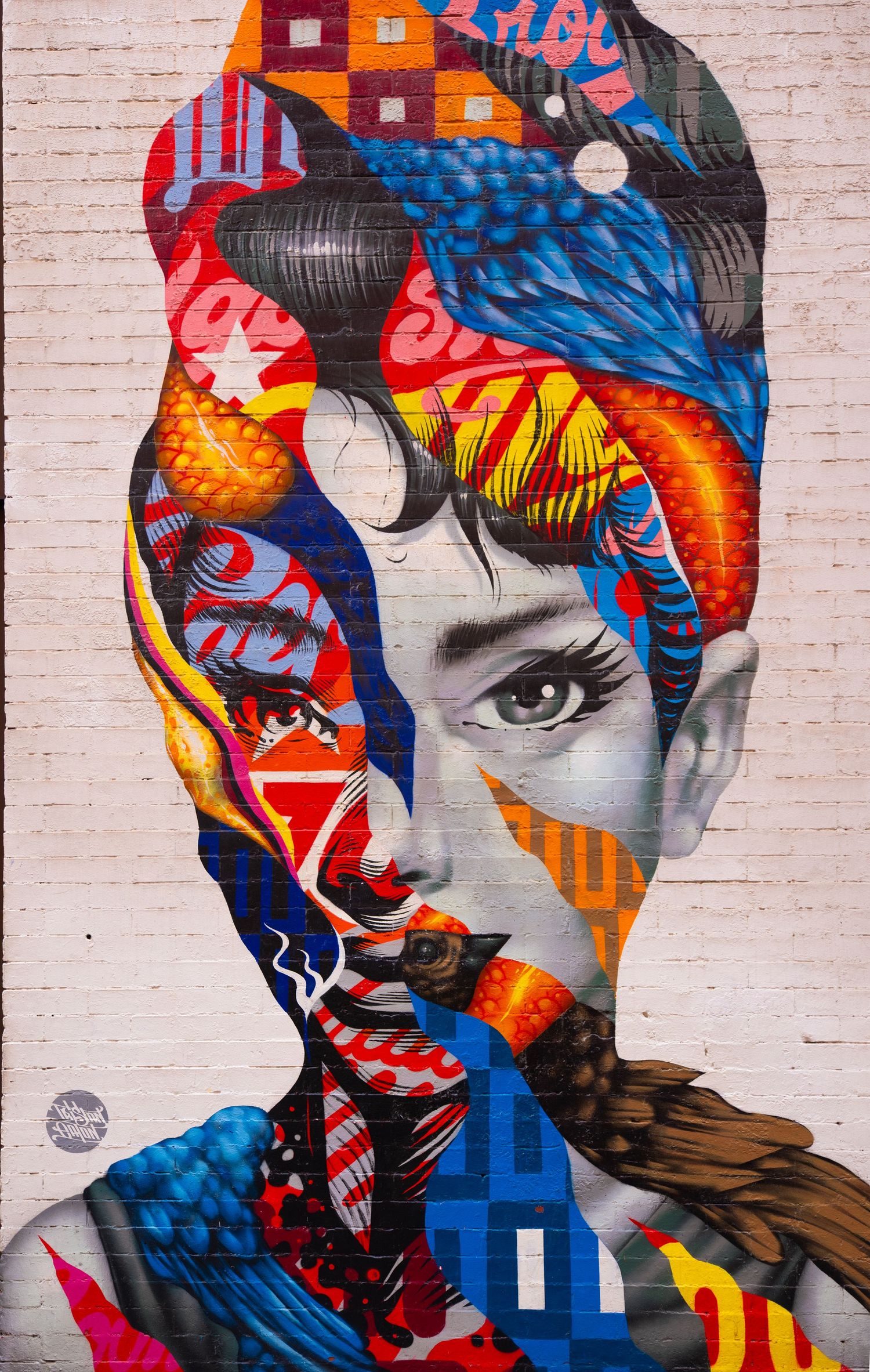 Vibrant street art mural featuring colorful geometric patterns on white brick wall.