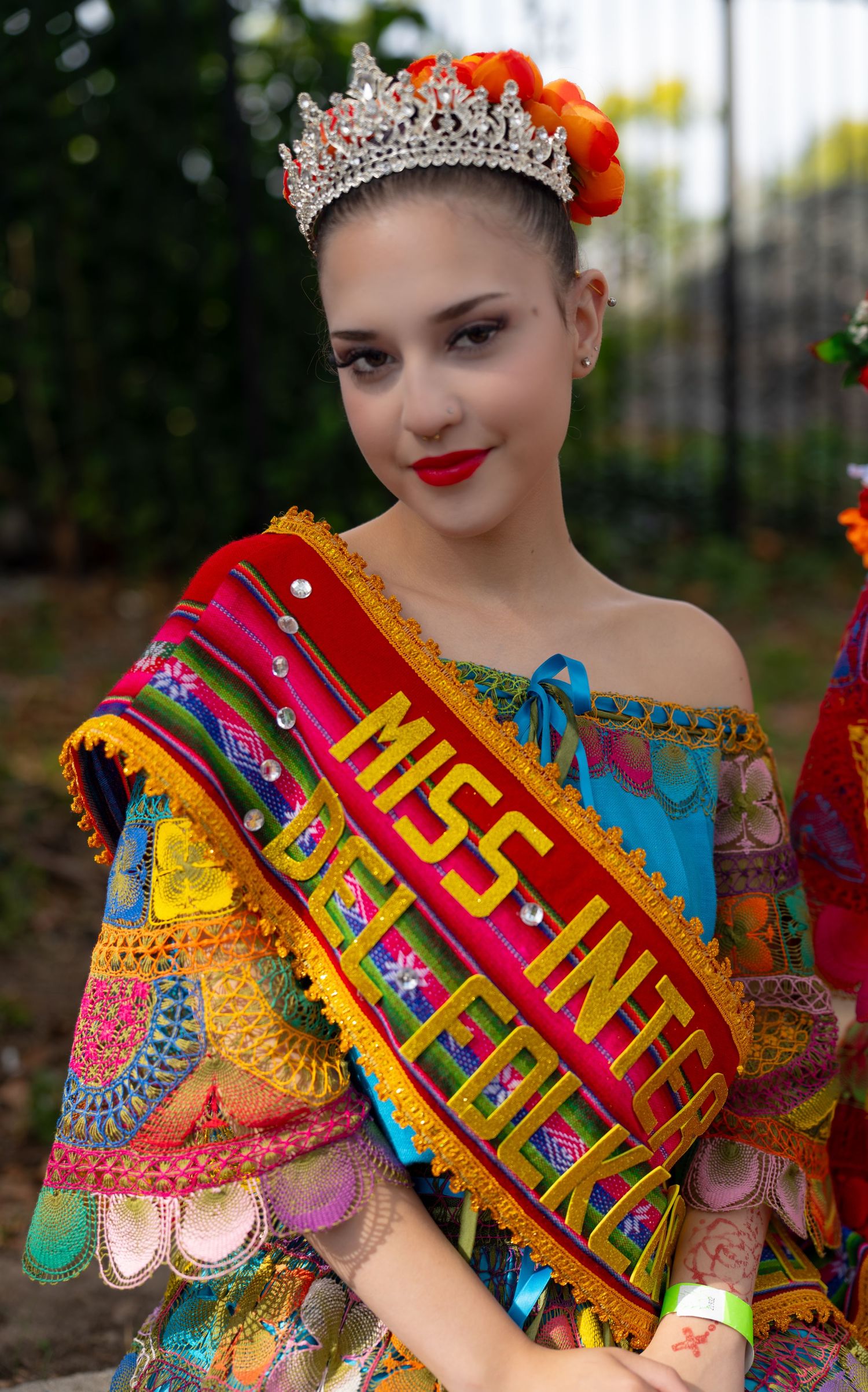 A pageant contestant wears a vibrant crown and sash with traditional colorful festival attire.