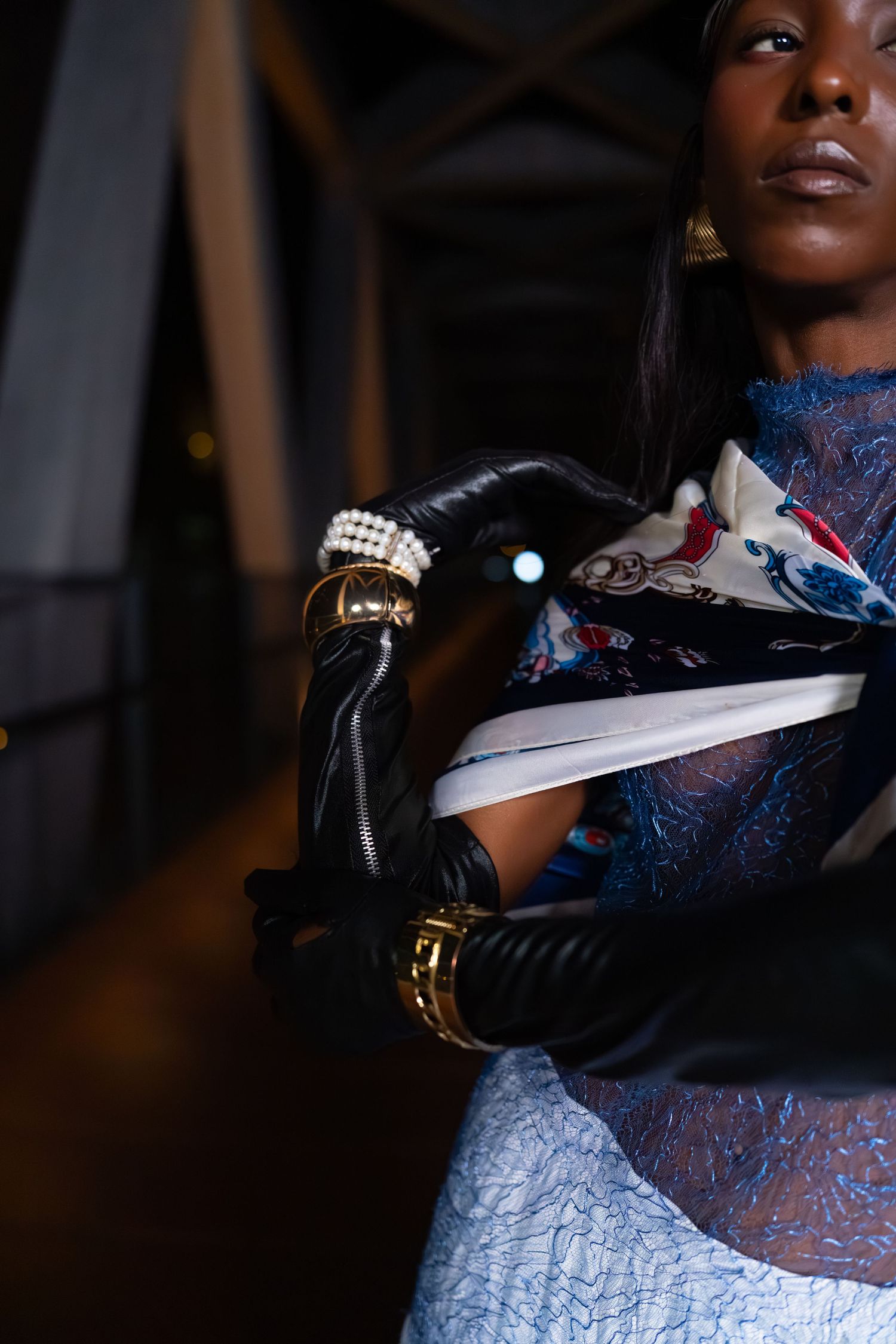 Fashion model wearing a light blue sparkly dress and black gloves poses in dramatic lighting for an editorial photoshoot.