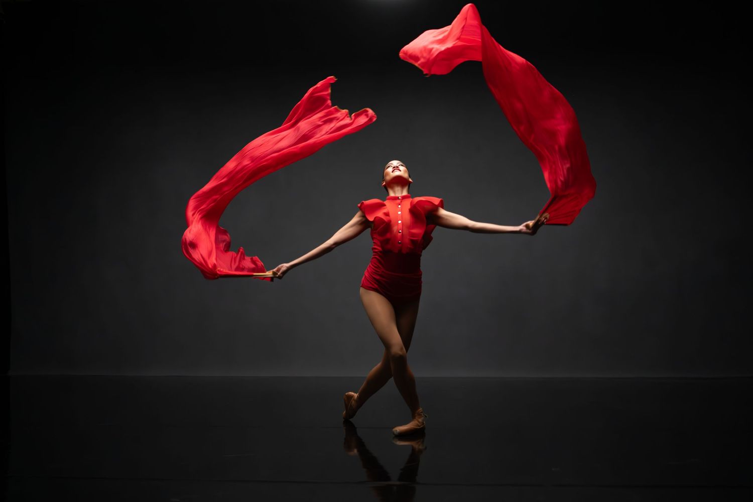 Dancer in red flowing fabric creates dramatic movement against dark background.