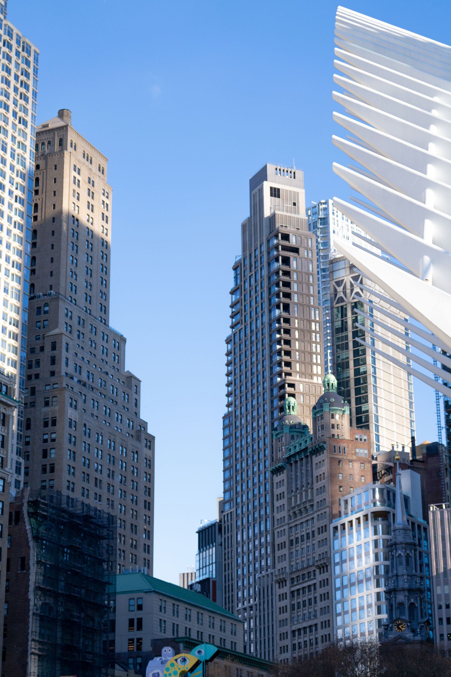 Modern skyscrapers and high-rise buildings tower against a bright blue sky in a bustling city skyline.