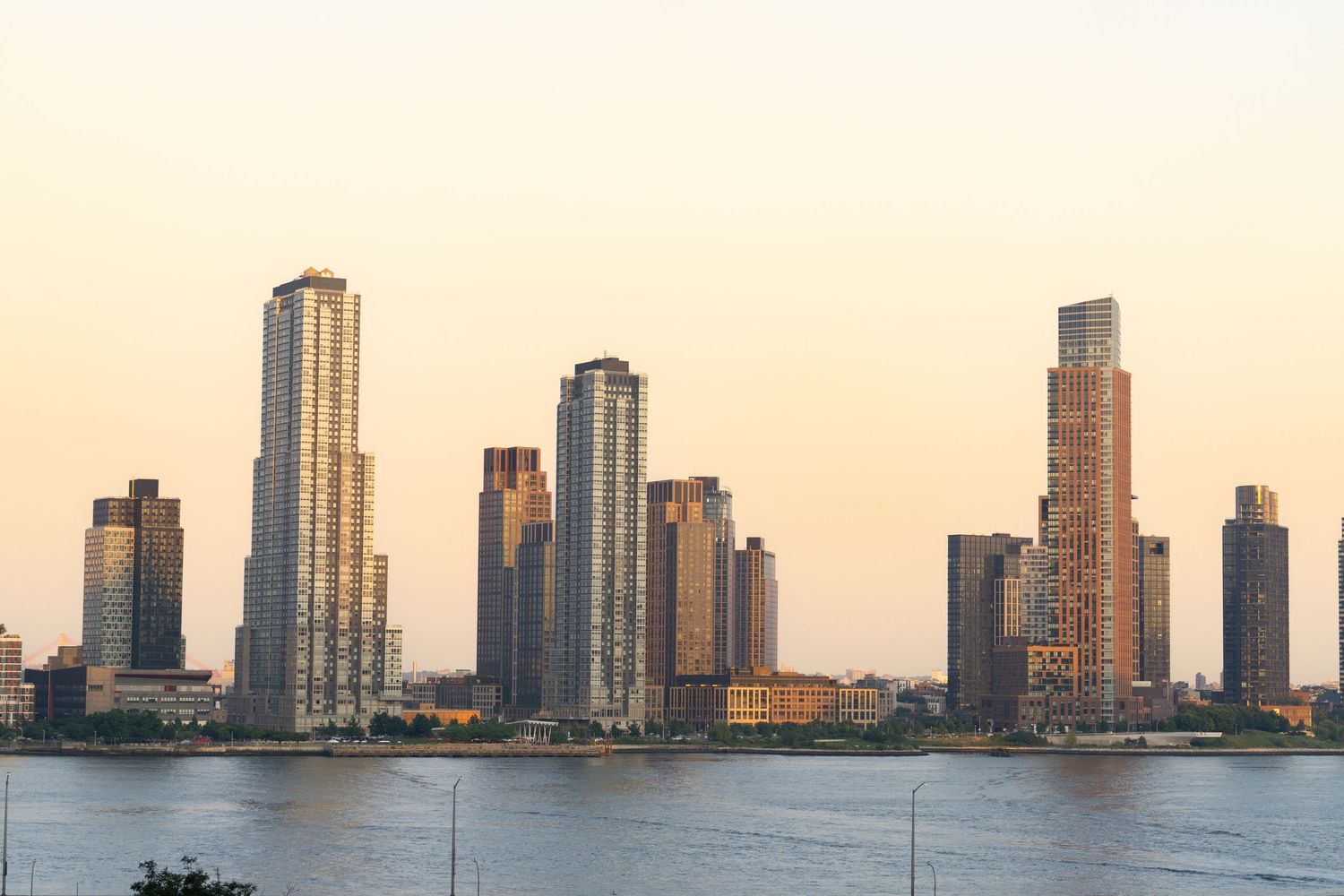 Modern waterfront skyline with tall residential skyscrapers reflecting golden sunset light.