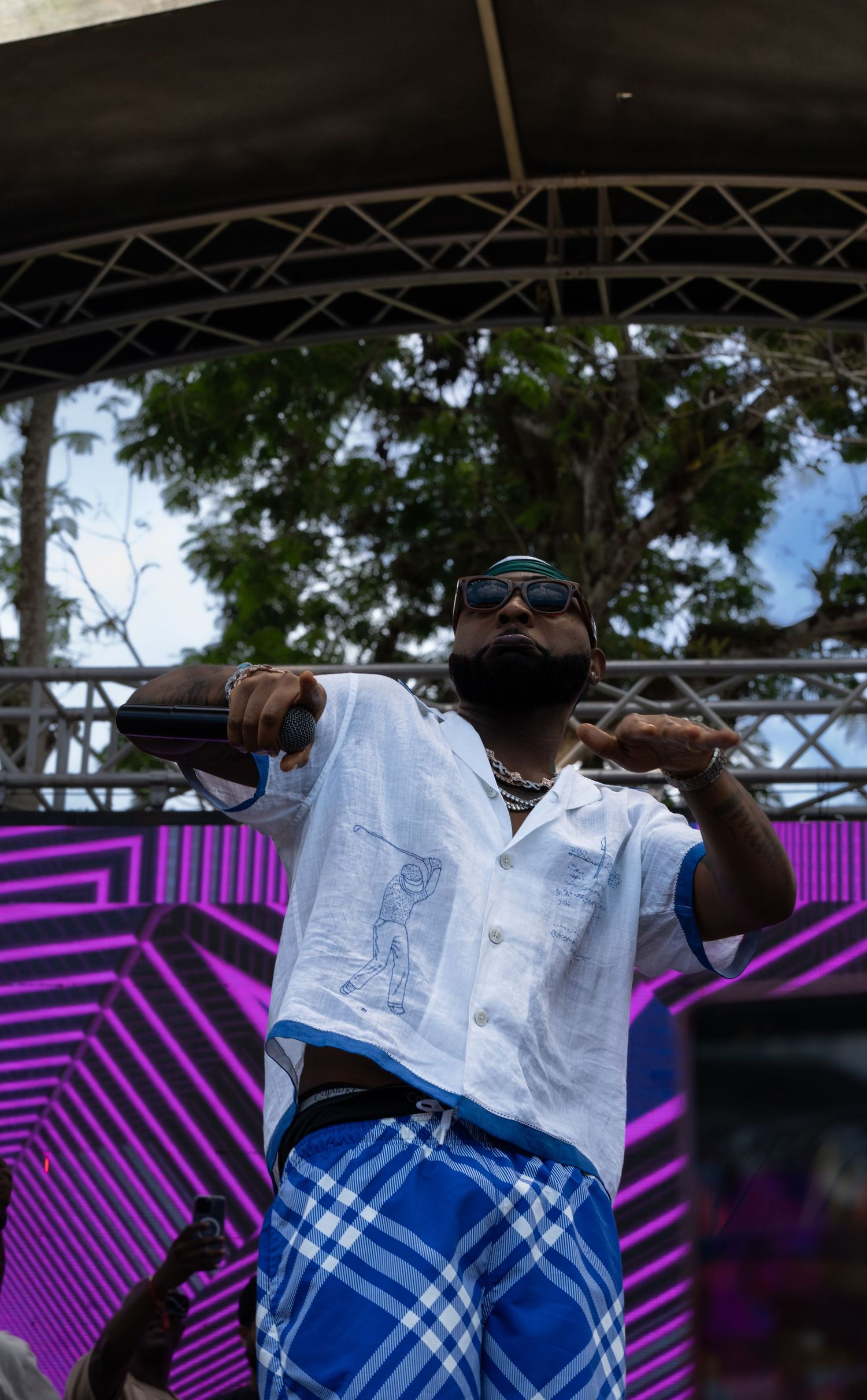 Artist performing on stage wearing white shirt and blue plaid pants with vibrant purple lighting.