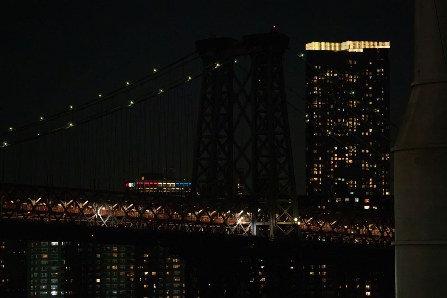 New York City nighttime skyline featuring illuminated buildings and bridge lights.