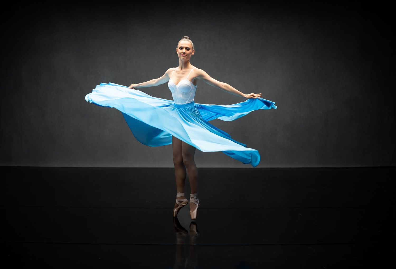 Performance artist creates dramatic shapes with flowing turquoise fabric on dark stage.