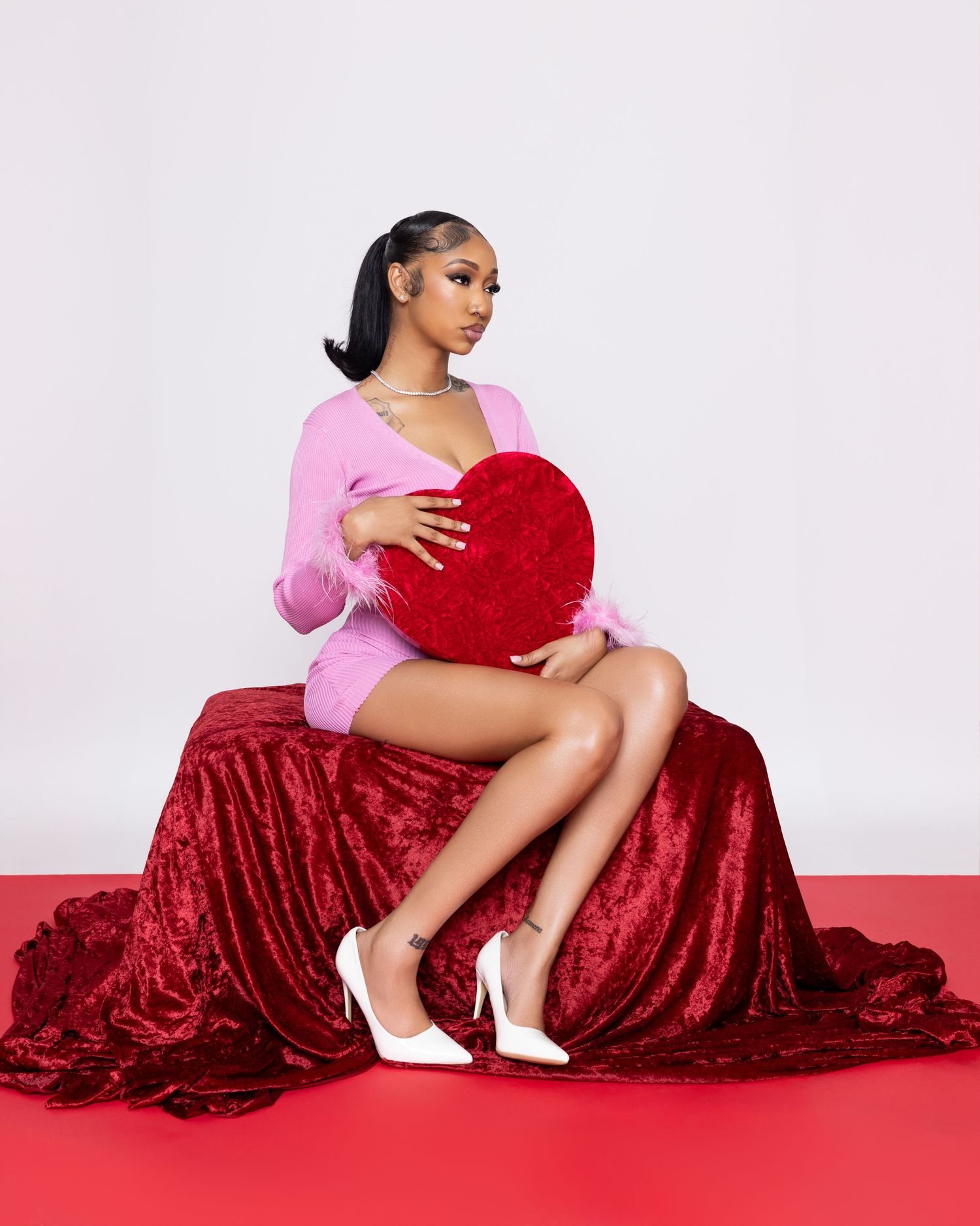 Artistic portrait series with model in pink top posing with red heart pillow on velvet backdrop.