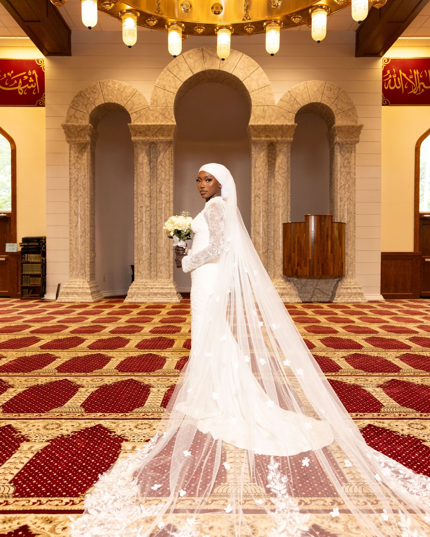 Elegant bridal photography in a mosque featuring long white veils and red carpet.