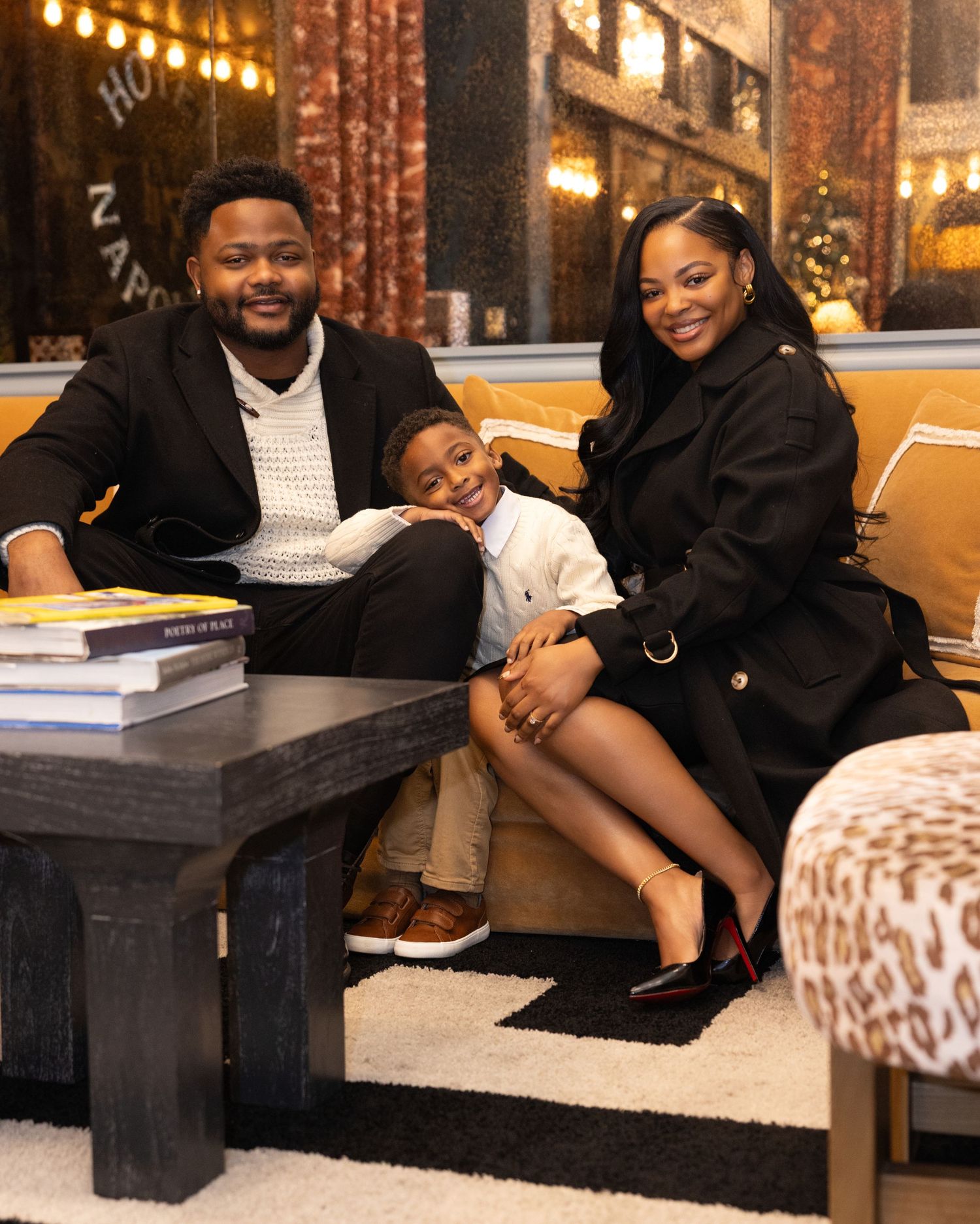 A family sits together on a couch in a warmly lit restaurant or lounge setting with books on a coffee table.