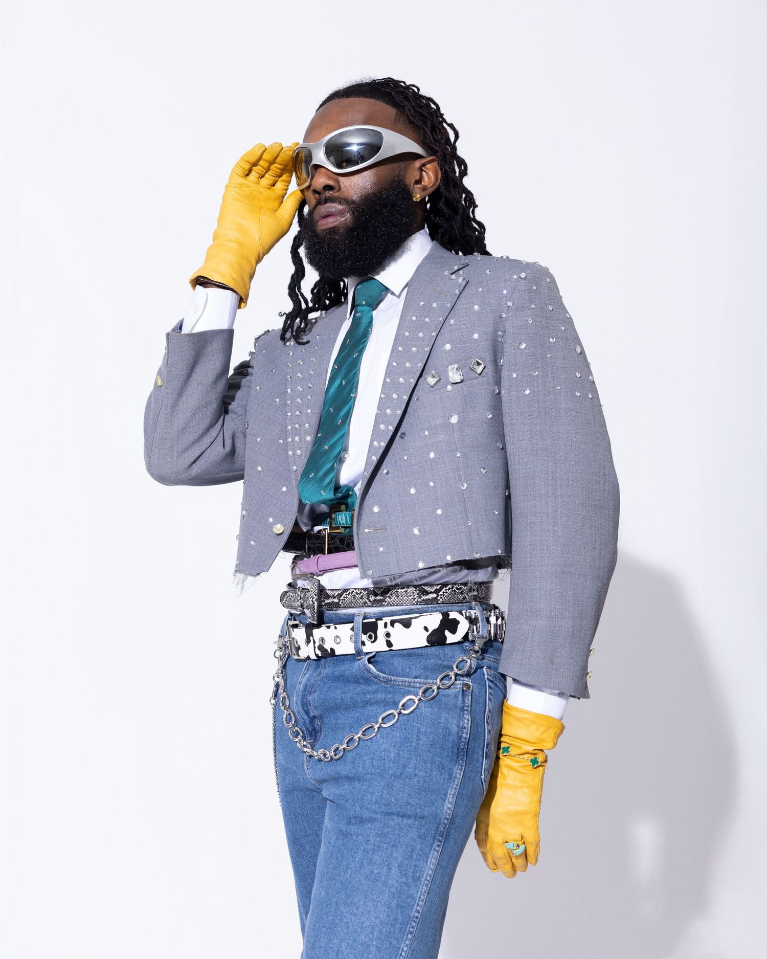 Fashion model in grey blazer and yellow gloves poses against white background.