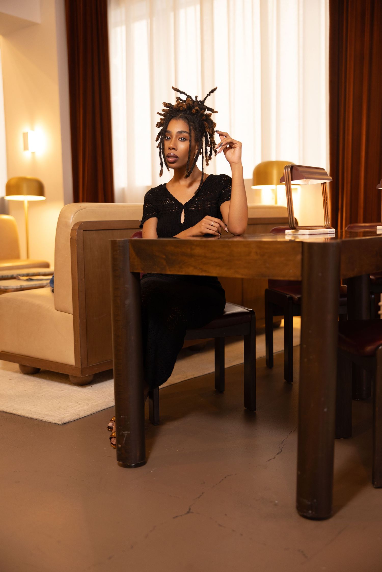 Model poses in a modern living room setting with dark furniture and warm lighting.