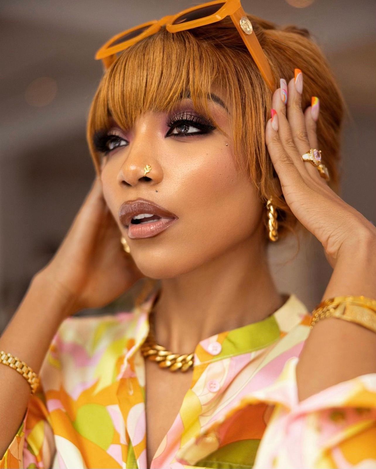 Fashion model wearing orange sunglasses and yellow floral top with glamorous makeup and gold jewelry.