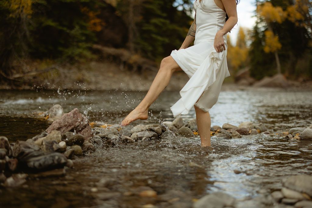 Bride wading barefoot in a mountain creek, by Sammy Aucella Photography