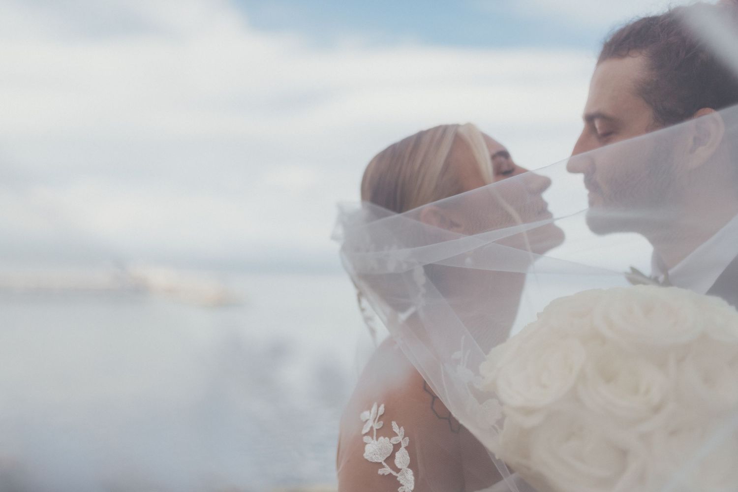 Couple sharing a soft moment behind the bride's veil by the coast, romantic elopement photography