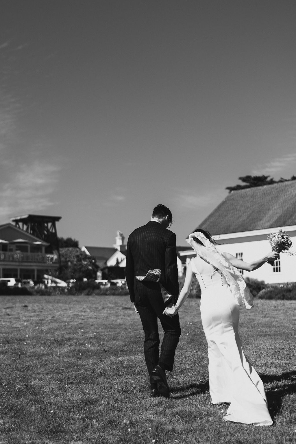 Black and white of the just-married couple walking a field at a MacCallum House Mendocino wedding, by Sammy Aucella Photography
