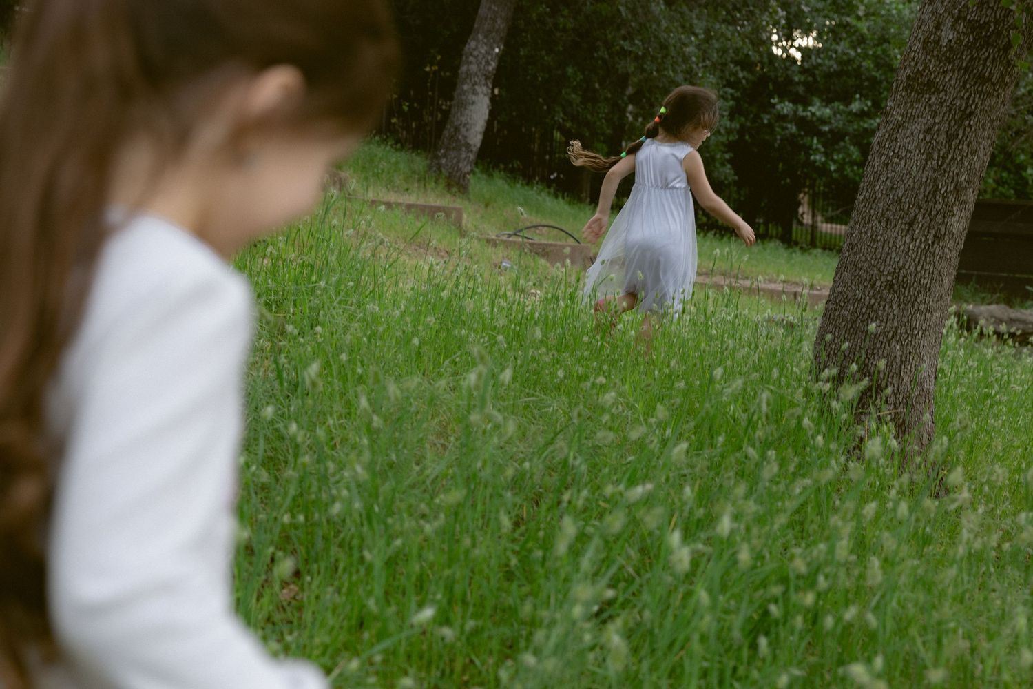 Young girl in the foreground as her sister runs through a grassy meadow behind, candid documentary family session