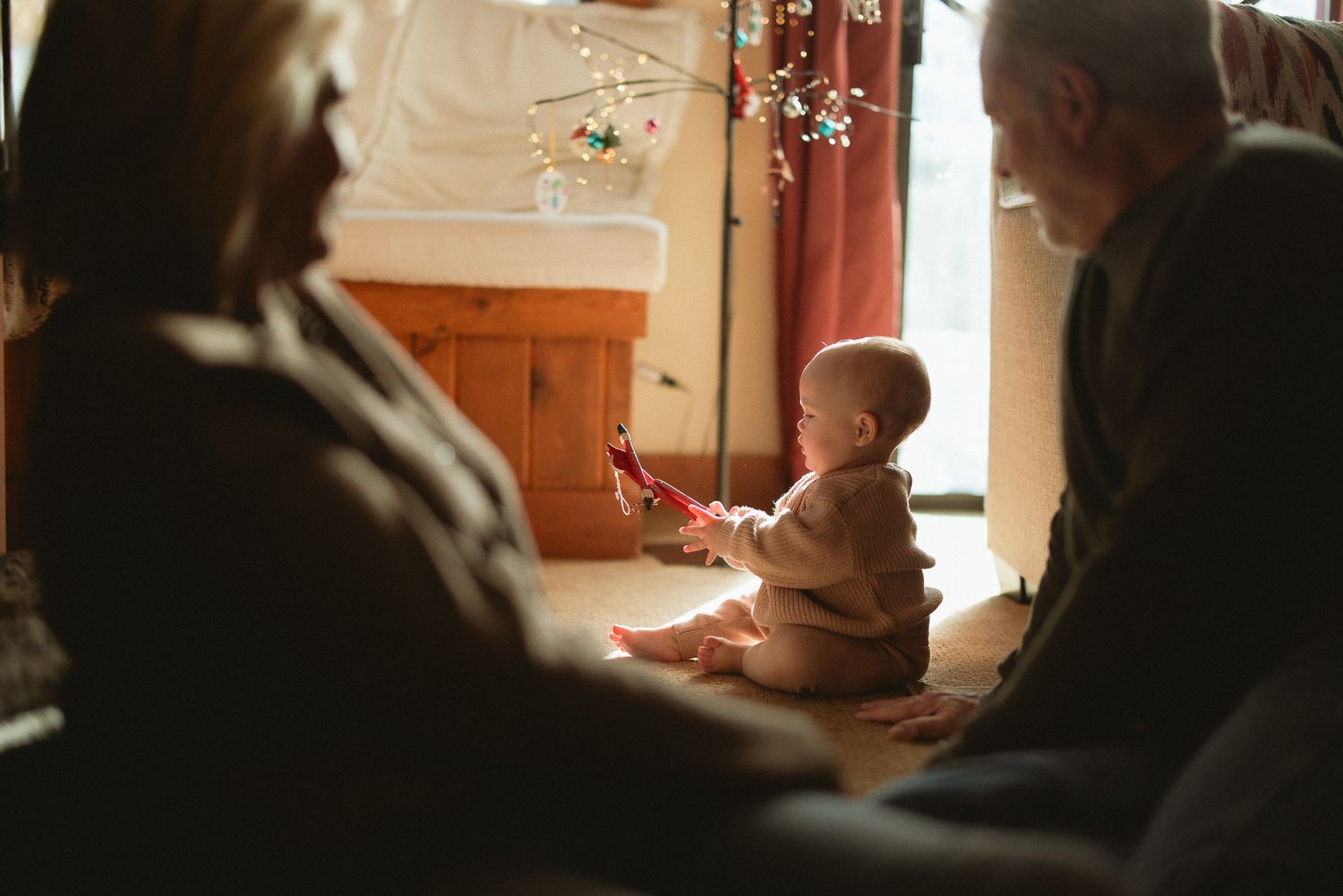 Baby playing on the floor between parents in a warm sunlit room, heartfelt indoor family session