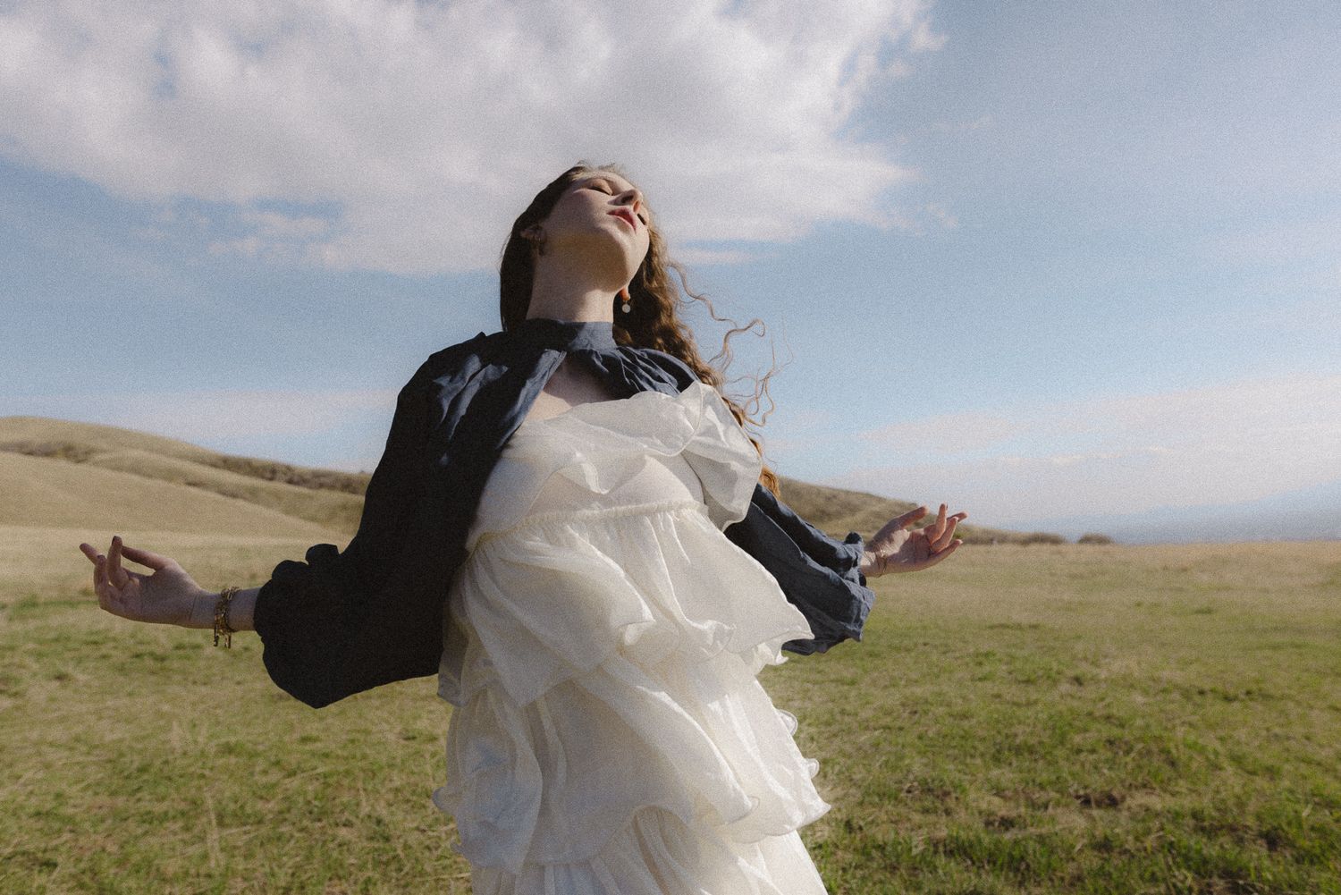 Bride with arms outstretched and head back in joy in an open grassy field under a big sky, free-spirited elopement portrait