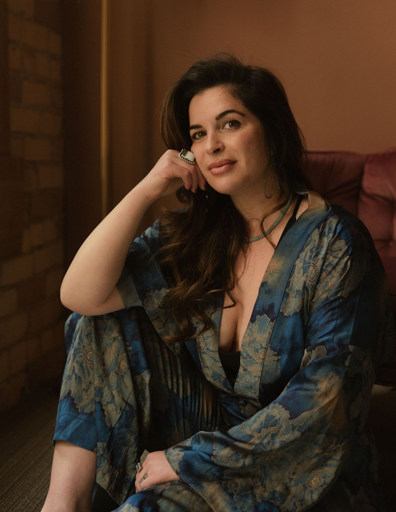 Wedding photographer Sammy Aucella seated in a patterned robe in a warmly lit room, editorial brand portrait
