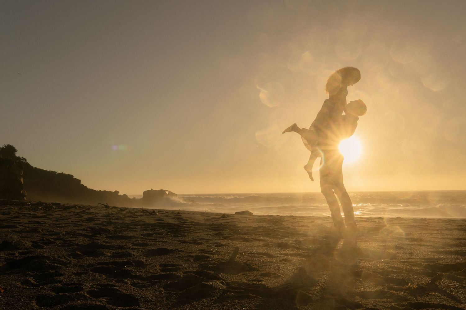 Couple running on beach at sunset silhouetted against golden California coastline during engagement session in Gualala California Mendocino