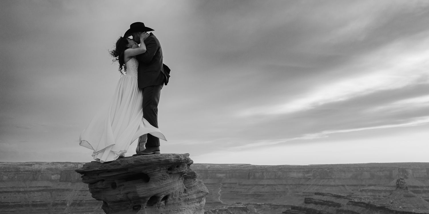 Black and white couple embracing on a cliff edge at Dead Horse Point in Moab, Utah, by Sammy Aucella Photography