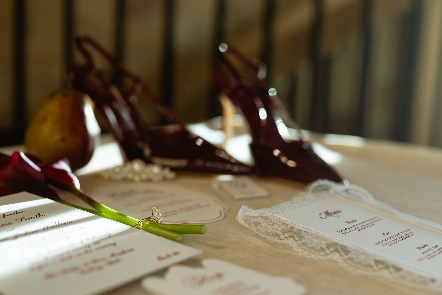 Wedding day flat lay with burgundy heels, calla lilies, a pear and the invitation suite on a table, elegant detail shot