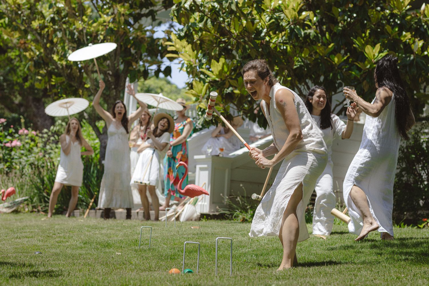 Wedding guests dressed in white playing lawn games with parasols at a festive garden reception, candid celebration