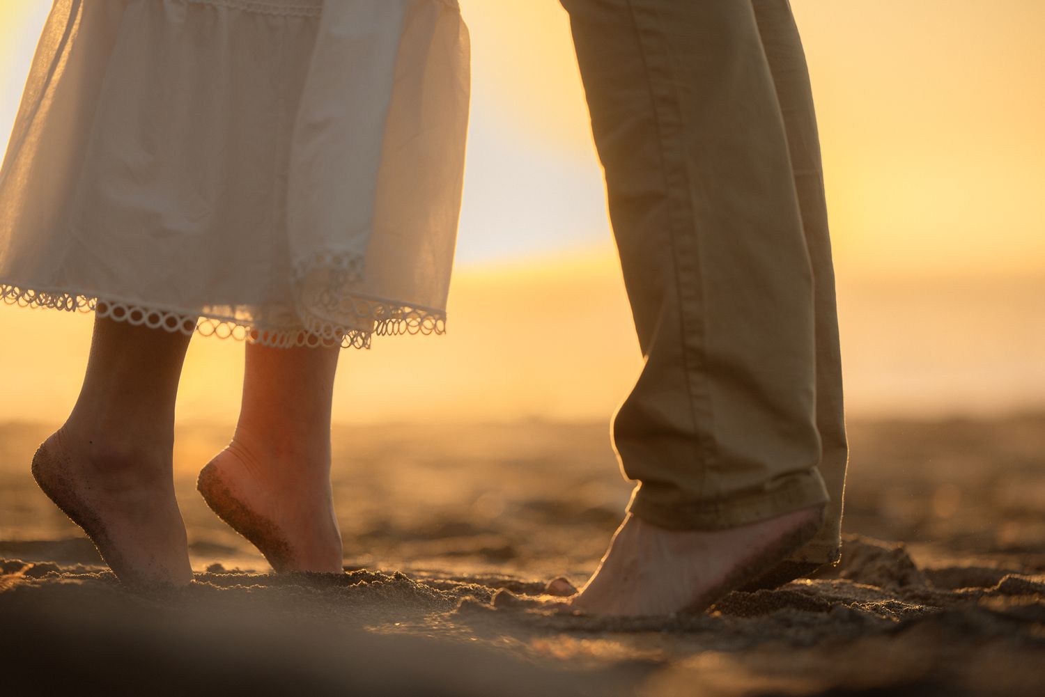 Close-up of a couple's bare feet standing together on the sand at golden hour, tender coastal elopement detail