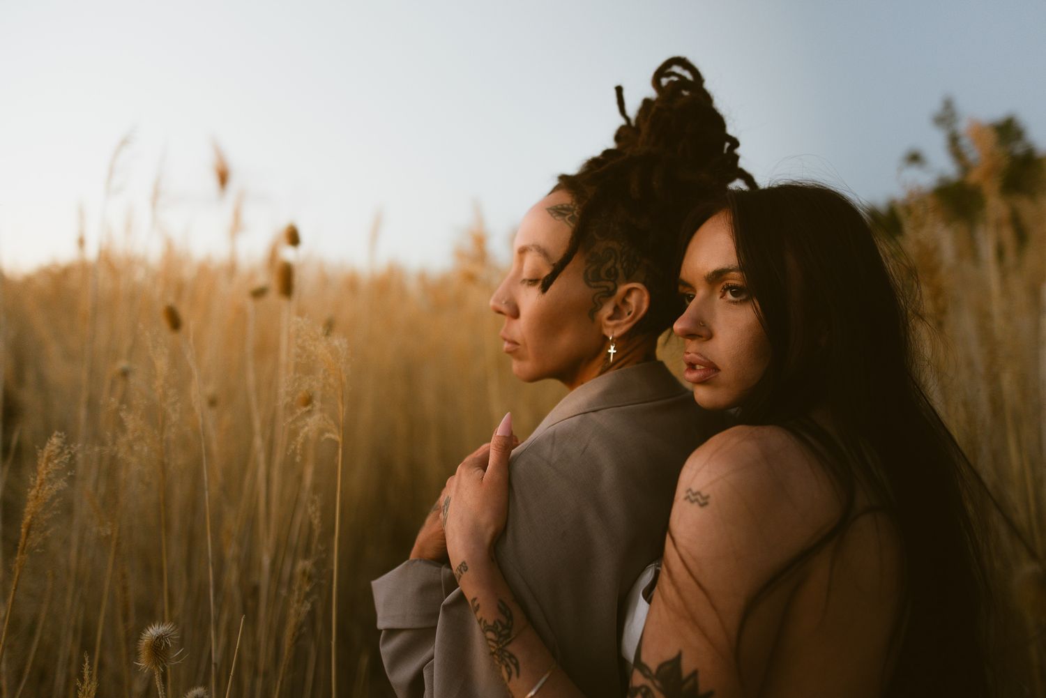 Lesbian couple back to back in a golden field at a Utah adventure session, by Sammy Aucella Photography