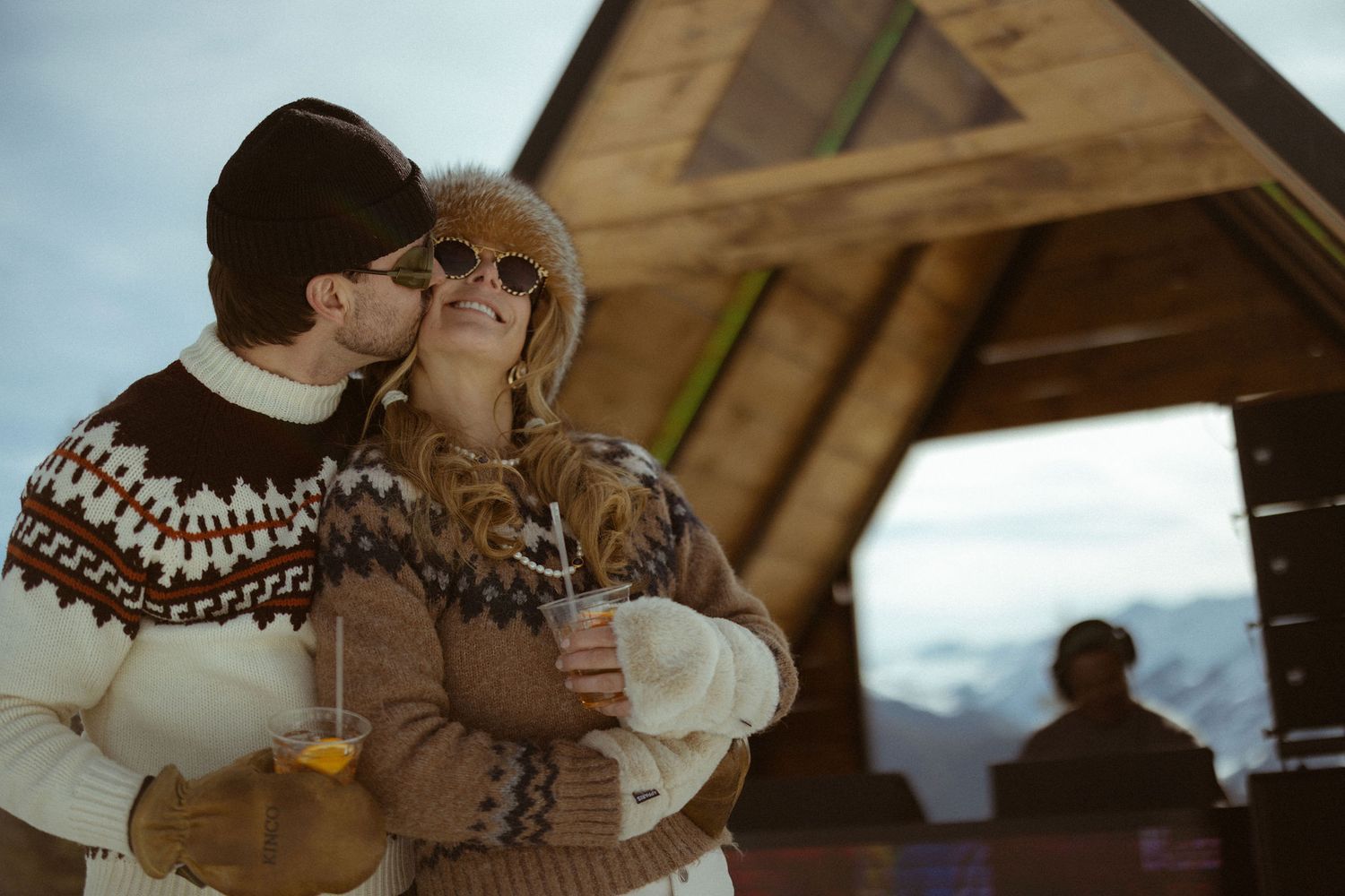 Couple in matching vintage ski sweaters embracing at Aspen ski lodge during unique engagement session by Sammy Aucella Photography