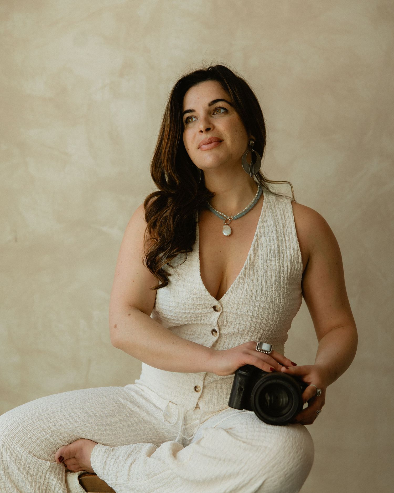 Wedding photographer Sammy Aucella in a white outfit holding her camera, relaxed studio brand portrait
