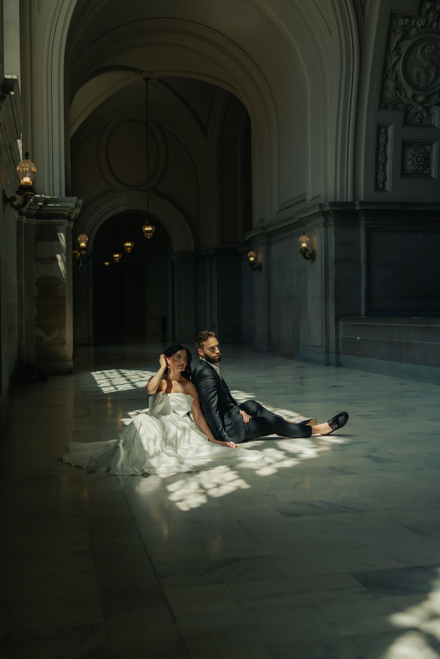Couple on the floor of a grand hallway in dramatic light at a San Francisco City Hall elopement, by Sammy Aucella Photography