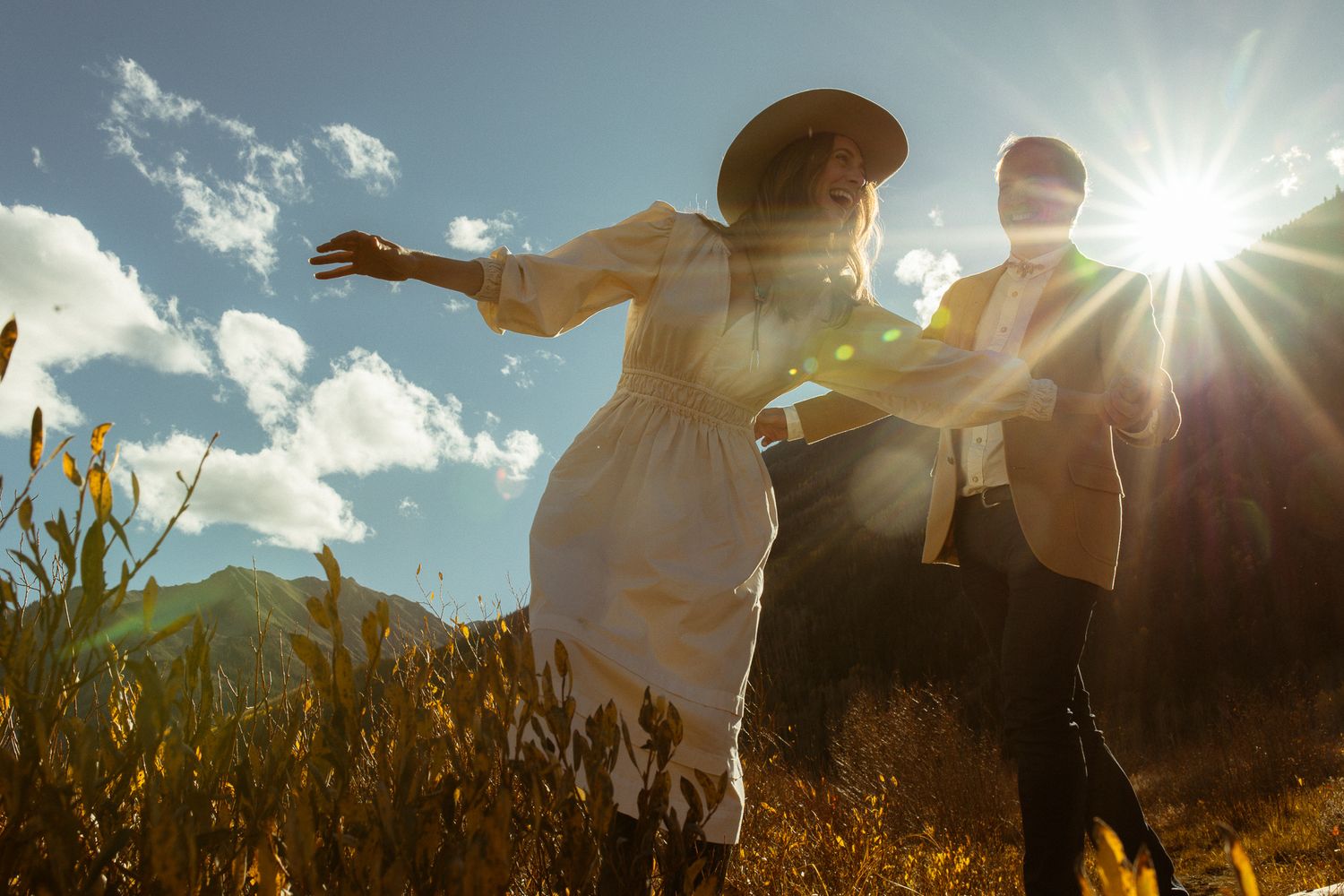 Couple spinning together in a sunlit field with a bright sun flare, joyful elopement photography