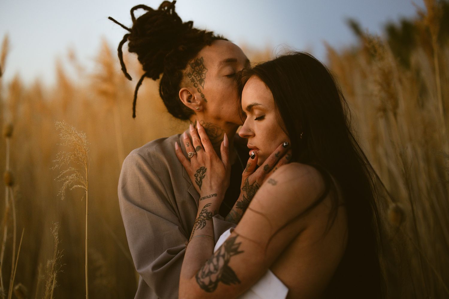 Couple embracing cheek to cheek in a golden field of tall grass at sunset, warm and intimate engagement session